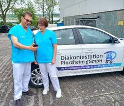 Mitarbeiter und Mitarbeiterin stehen vor Auto Diakoniestation