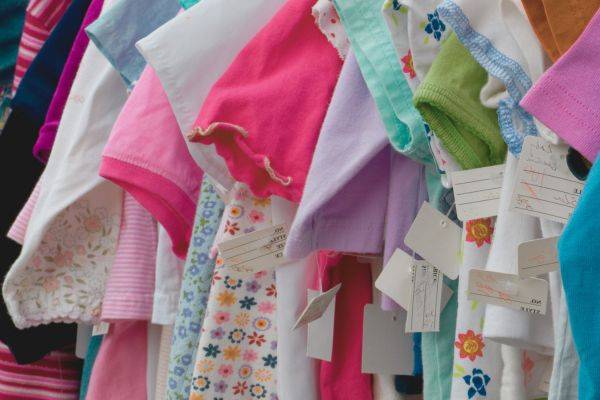 Kinderkleier hängen an einer Kleiderstange, Schrift: Kinderflohmarkt