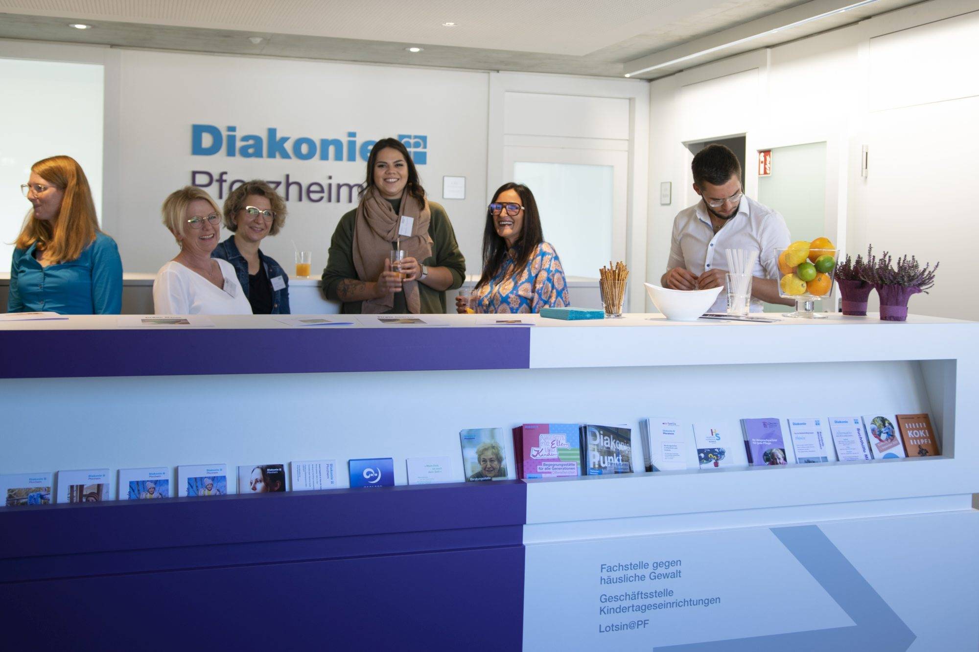 Quelle: ©EvKirchePF Menschen hinter einer Bar, im Hintergrund das Logo der Diakonie Pforzheim