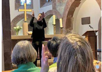 Gebärdendolmetscherin steht vor Altar, 3 Frauen von hinten in Kirchenbank sitzend
